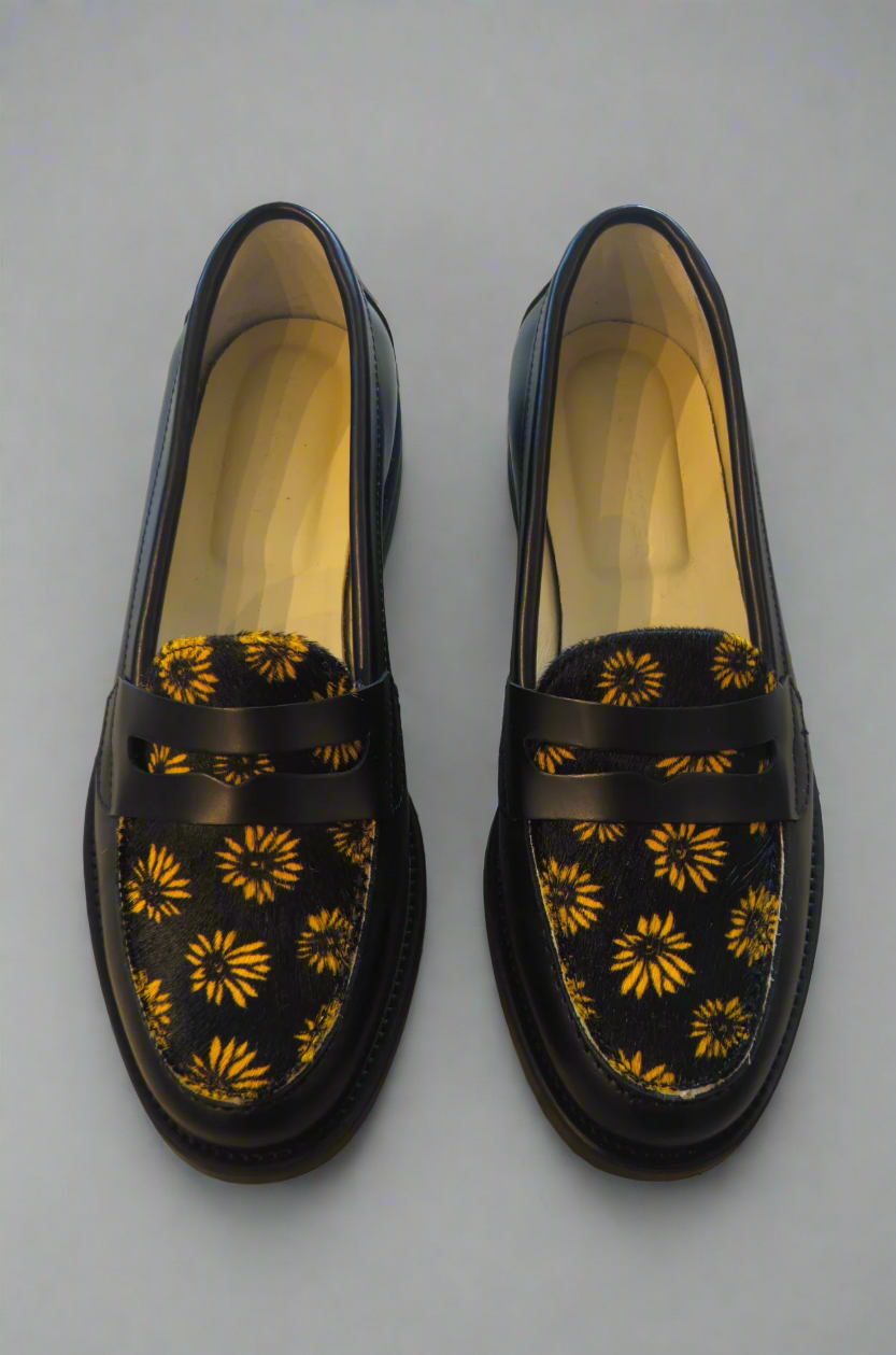 Black loafers with yellow floral patterns on a concrete floor