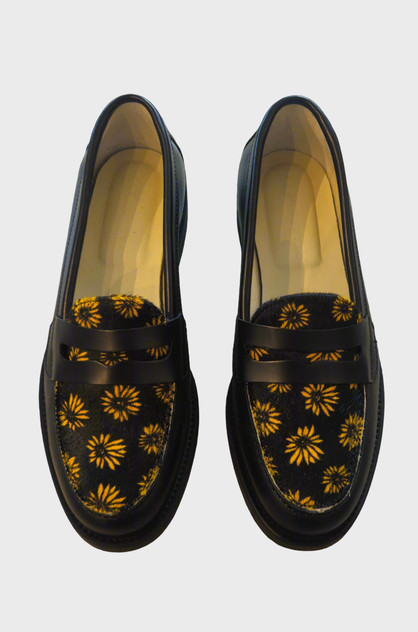 Black loafers with yellow floral patterns on a concrete floor