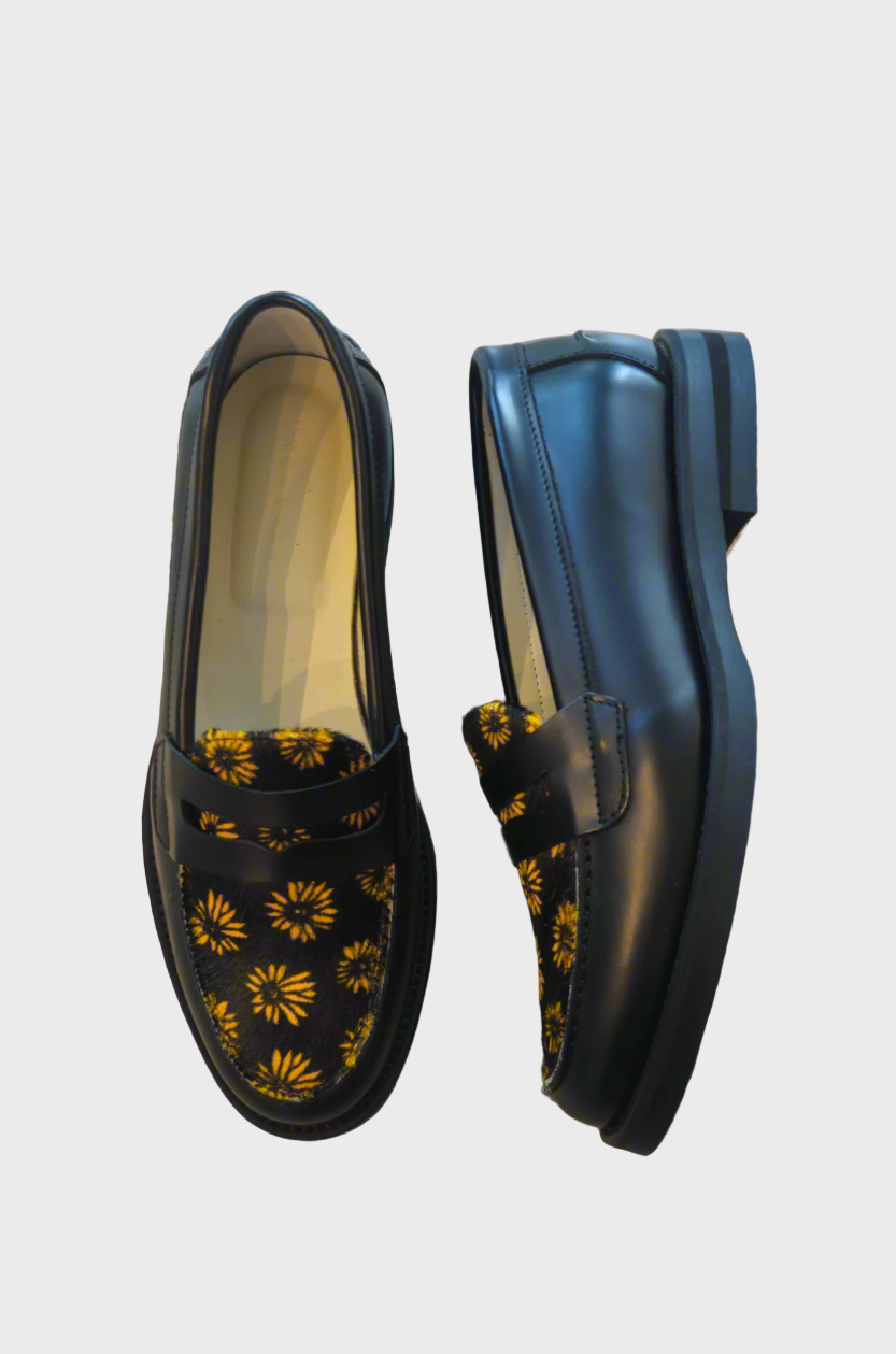 Black loafers with yellow floral patterns on a textured surface