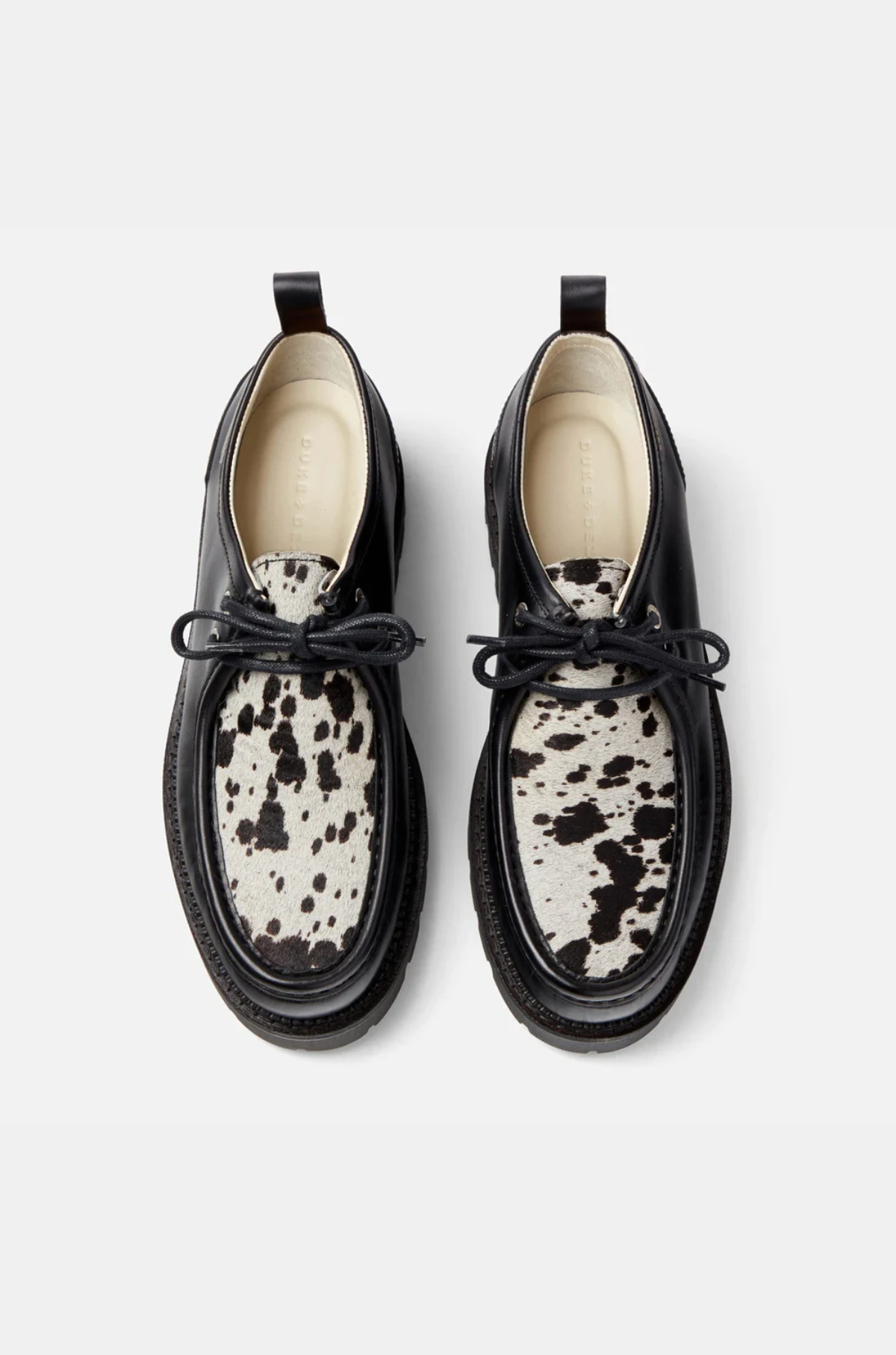Black leather shoes with white cow print soles on a light gray background