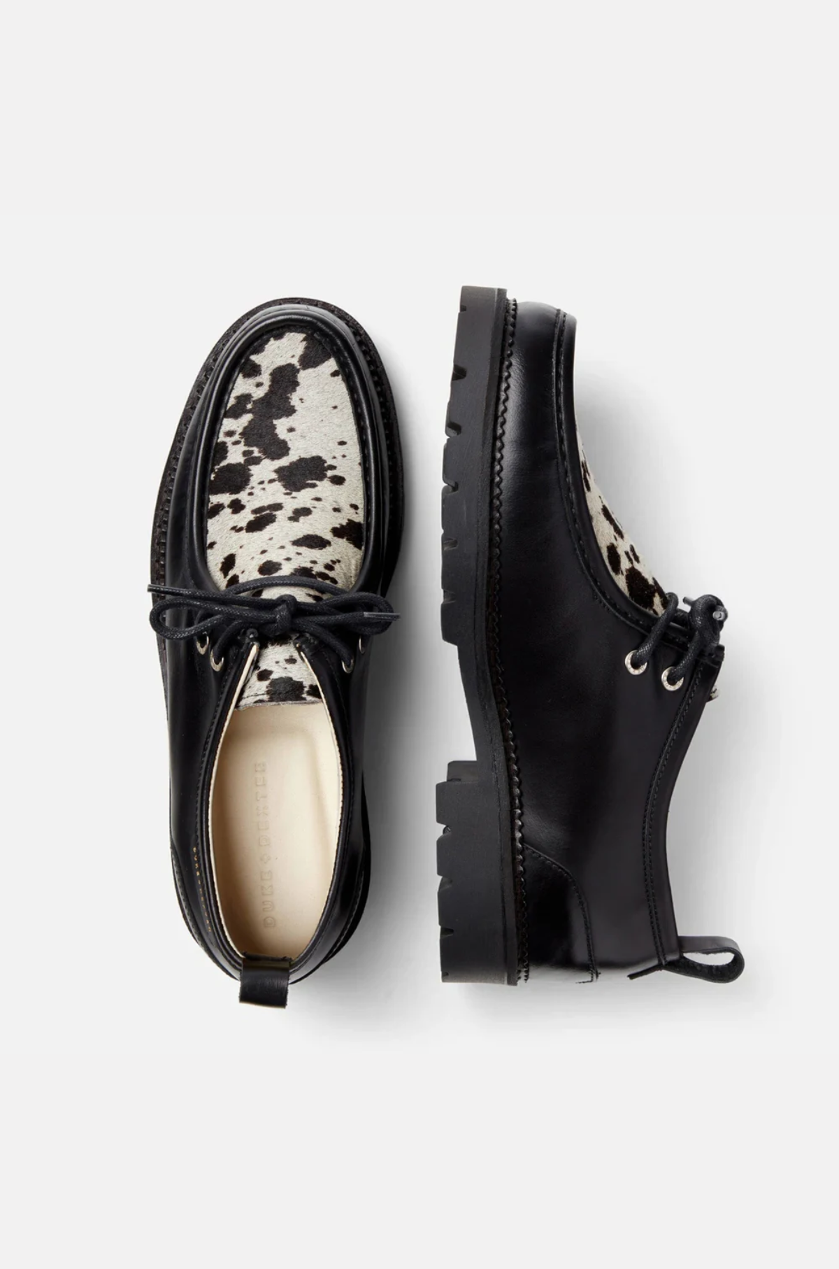 Black leather shoes with white cow print accents on a white background