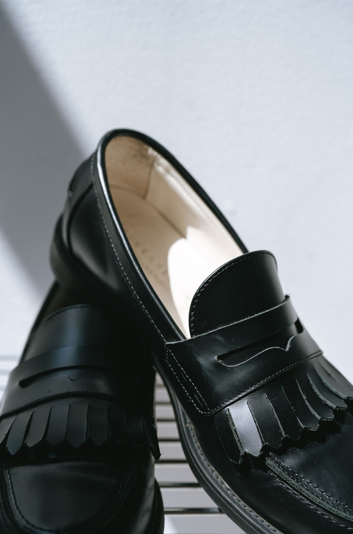 Black loafers with fringes on a light gray background with fringes