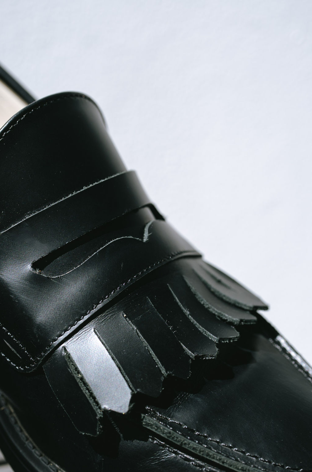 Close-up of a black leather shoe with a white background and fringes on the tongue