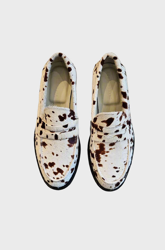 Pair of white loafers with black spotted pattern on a concrete floor