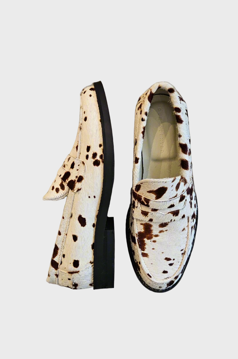 Pair of white loafers with black and brown speckles on a concrete surface