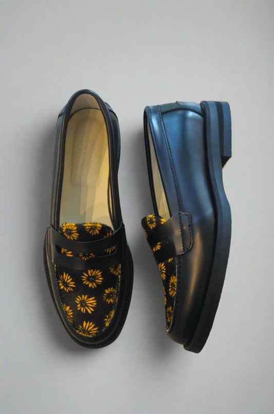 Black loafers with yellow floral patterns on a textured surface