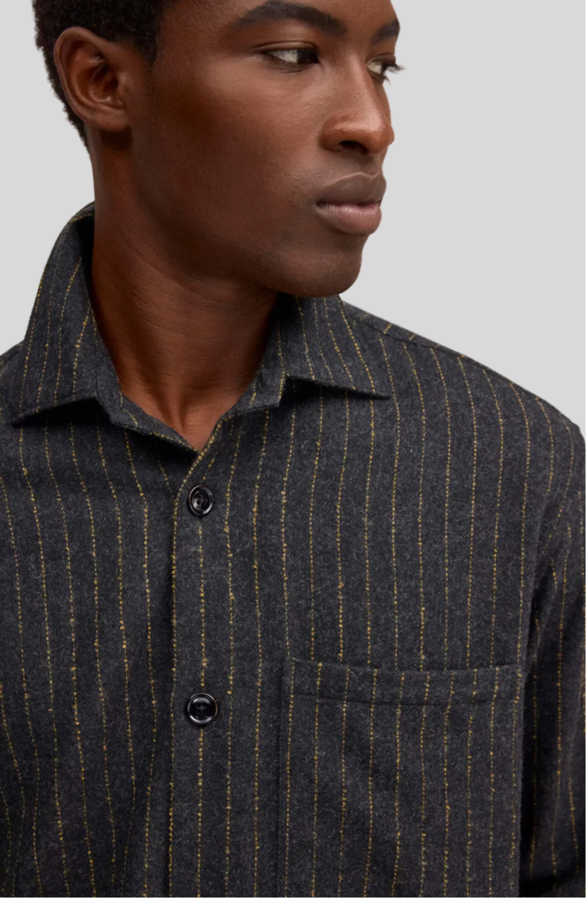 A close-up of a man wearing a dark charcoal gray button-down shirt with thin vertical gold pinstripes and a chest pocket.